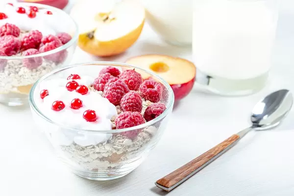 Oatmeal porridge with raspberries and red currant in bowl on white table