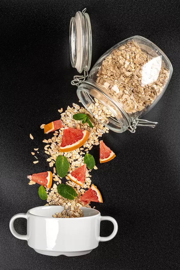 Oatmeal poured from a glass jar with pieces of grapefruit and mint on a dark background with a bowl