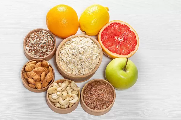 Oatmeal surrounded by nuts and seeds with fresh fruit on a white wooden background. Top view