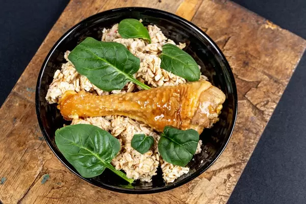 Oatmeal with baked chicken leg and green leaves on an old wooden kitchen board, top view
