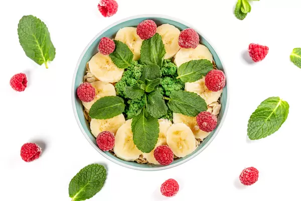 Oatmeal with banana slices, raspberries and mint on white, top view