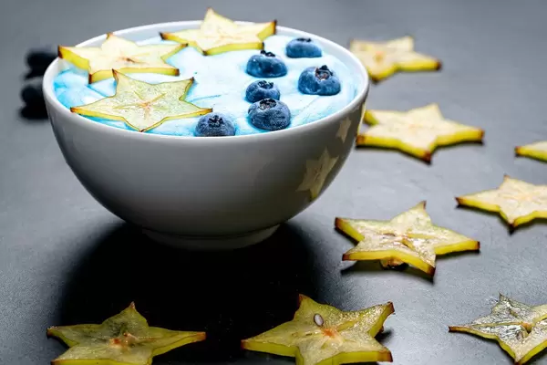 Oatmeal with carambola and blueberries in a white bowl on a black background with sliced carambola pieces (Flip 2019)