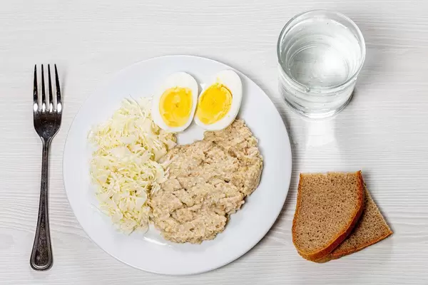 Oatmeal with fresh cabbage salad and boiled eggs on a white table with black bread and a glass of water (Flip 2019)