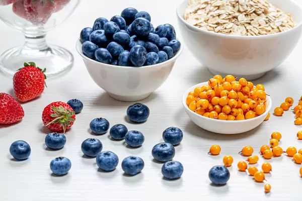 Oatmeal with fresh strawberries, sea buckthorn and blueberries in white bowls