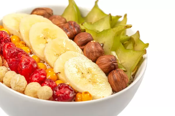 Oatmeal with slices of carom fruit, hazelnuts, banana, sea buckthorn and dried cherry, close-up