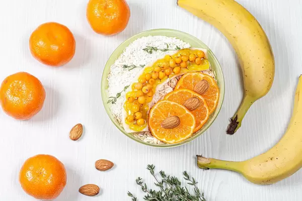 Oatmeal with slices of Mandarin, banana, sea buckthorn berries, almonds and coconut on a white wooden background (Flip 2019)