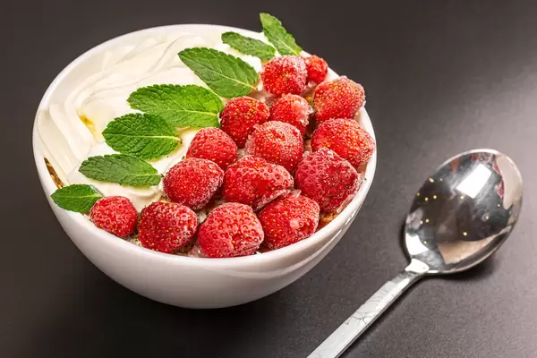 Oatmeal with strawberries and mint leaves, close-up on black background