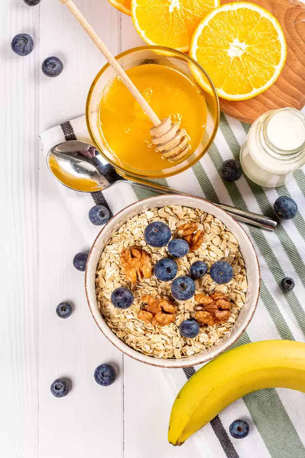 Oatmeal with walnuts and blueberries on a table with milk, honey, banana and orange