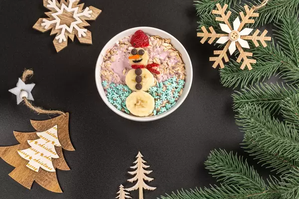 Oatmeal with yogurt and snowman made from slices of banana and strawberry on christmas background