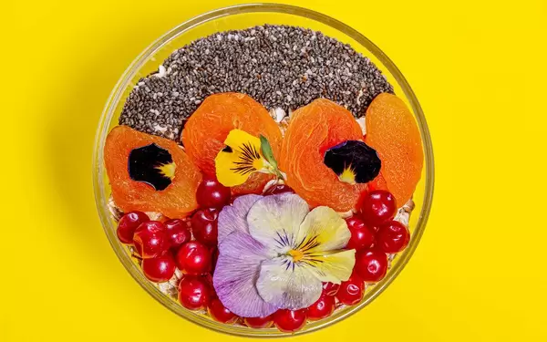 Obene Aufnahme von einer Schüssel mit Haferflocken, Beeren, Chiasamen und essbaren Blumen