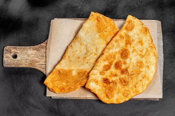 Obene Aufnahme von frisch gebratenem Chebureki auf schwarzem Tisch