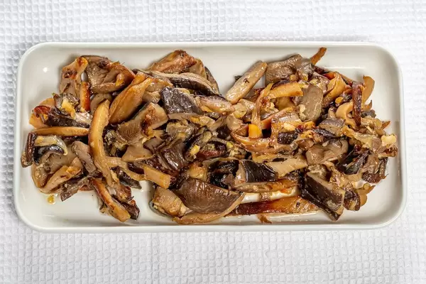 Obene Aufnahme von gebratenen Austernpilzen mit Zwiebeln auf einem weißen Küchentuch