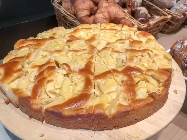 Obstkuchen in Kuchenstücken geschnitten, auf einem runden Holzteller am Büfett, mit Backwaren im Hintergrund