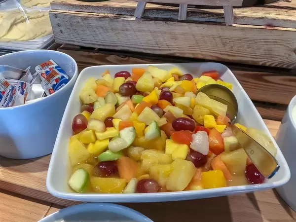 Obstsalat mit Melone, Trauben, Mango und Ananas, in einer weißen Schale mit Löffel an einem Büfett