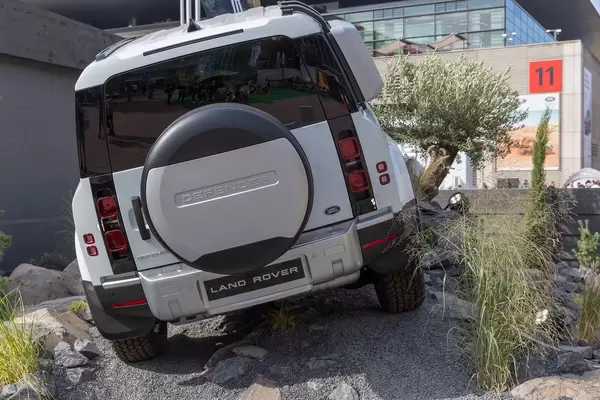 Off-road vehicle Land Rover Defender mit spare tire outside in rough terrain, with in-car infotainment system Pivi Pro