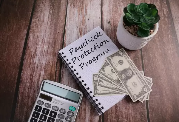 Office desk table with calculator and notebook with Paycheck Protection Program text