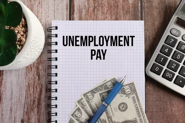 Office desk table with calculator and notebook with Unemployment Pay text
