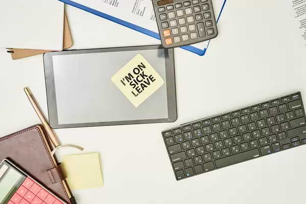 Office workplace and a sticky note on the tablet with text - I am on sick leave