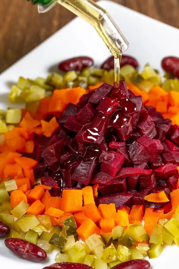 Öl fließt aus einer Flasche in einen bunten Gemüsesalat