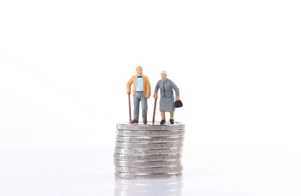 Old couple standing on top of stack of coins on white background