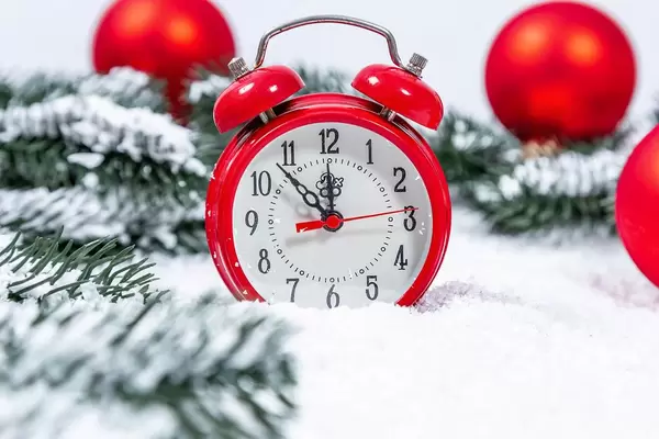 Old-fashioned red alarm clock in winter setting with artificial snow and Christmas decoration