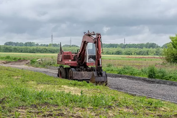 Old red excavator on the road in the field