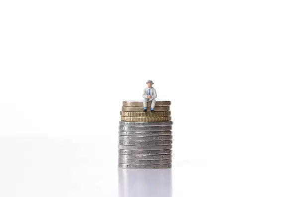 Older man sitting on a stack of coins on white background