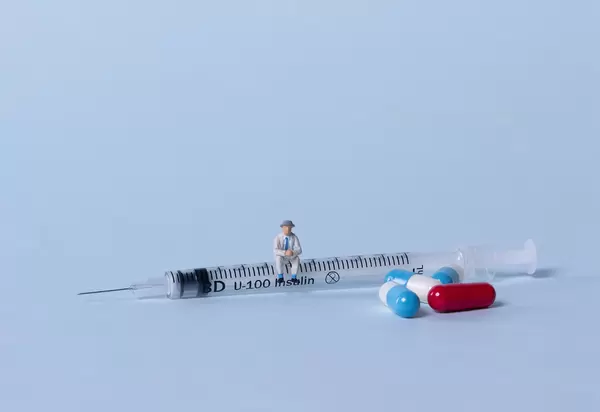 Older man sitting on a syringe and pills on light blue background