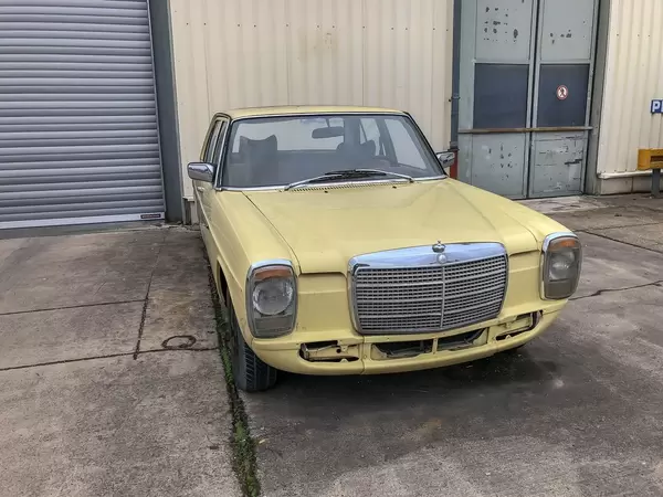 Oldtimer Auto Mercedes 200D in hellgelb steht vor Garageneinfahrt