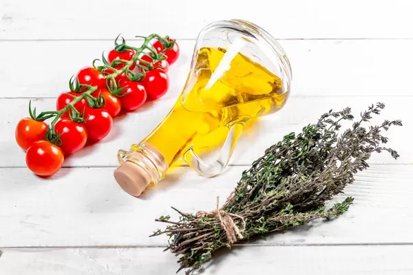 Olivenöl in einer Karaffe, Tomatenstaude und gebundene Thymian-Kräuter, liegend auf einem weißen Holztisch