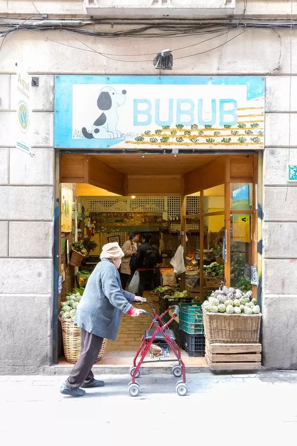 Oma mit Rollator passiert den spanischen Gemüsehändler Bubub an der Carrer de Joaquín Costa Fußgängerzone in Barcelona, Spanien