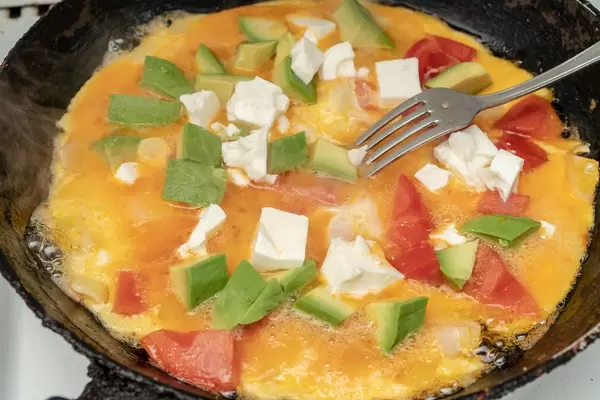 Omelet with Avocado Cheese and Tomatoes in the frying pan