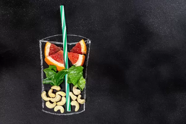 On a black background chalked glass with pieces of fresh grapefruit, lettuce and cashews. Top view with free space (Flip 2019)