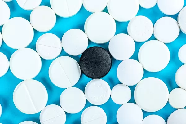 One black pill and many white pills on a blue background