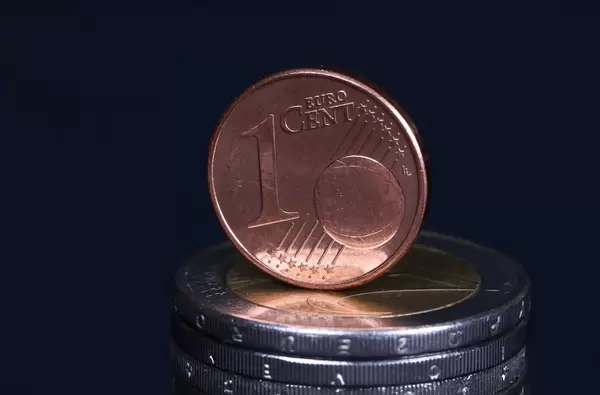 One Euro cent coin placed on top of piles of Two Euro coins