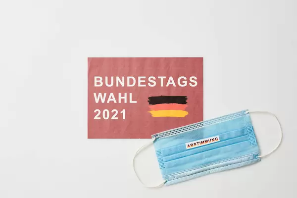 OP-Maske mit Schrift "Abstimmung". Roter Zettel mit deutscher Flagge und Schrift "Bundestagswahl 2021"