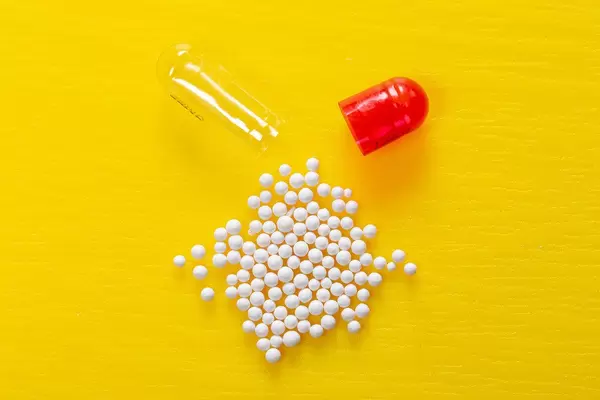 Open capsule and white drug granules on yellow background (Flip 2019)