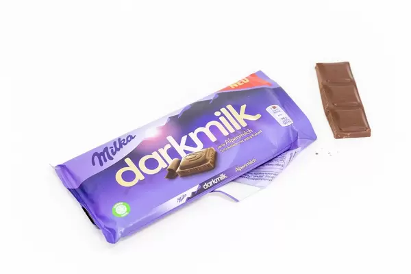 Open chocolate bar packaging of "Milka darkmilk" made of alpine milk, on a white table