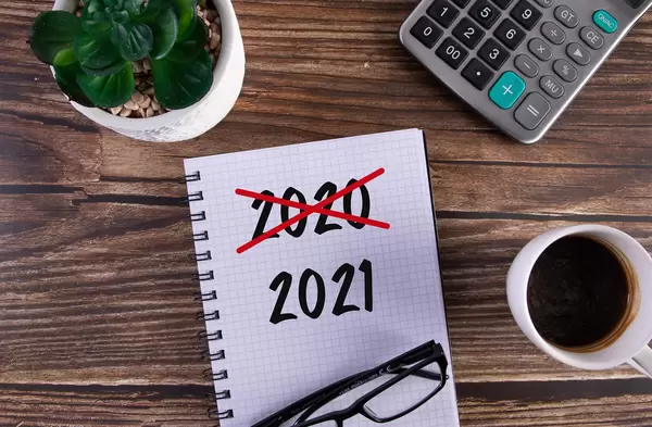 Open notebook with crossed 2020 text and 2021 text on wooden table