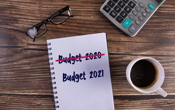 Open notebook with crossed Budget 2020 text and Budget 2021 text on wooden table