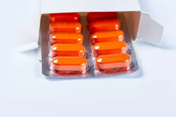 Open package with orange capsules on a white background