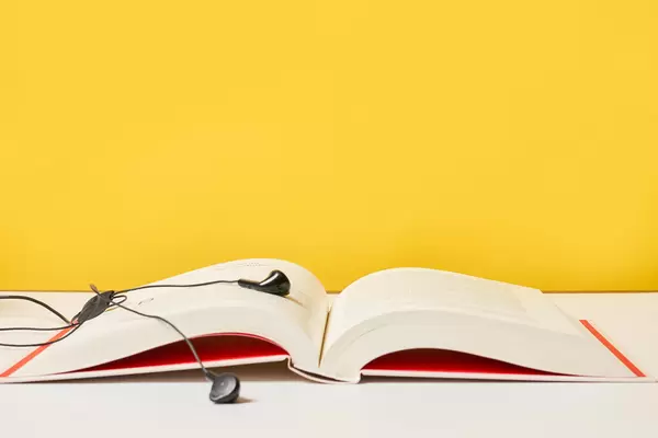 Open page of a book and earphones against the yellow background