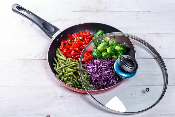 Open pan with lid with vegetables inside on white wooden background