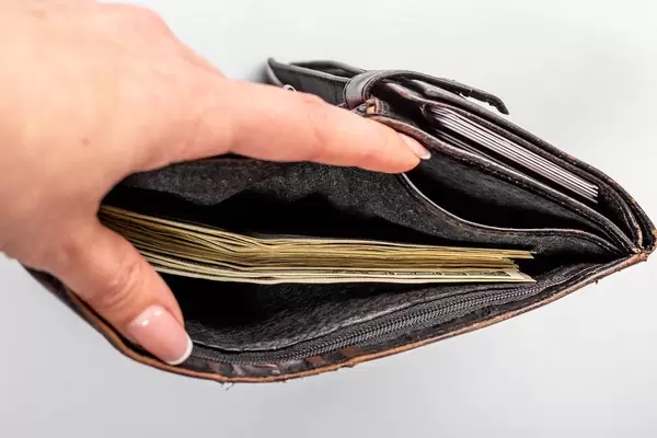 Open wallet is full of money with female hand on white background