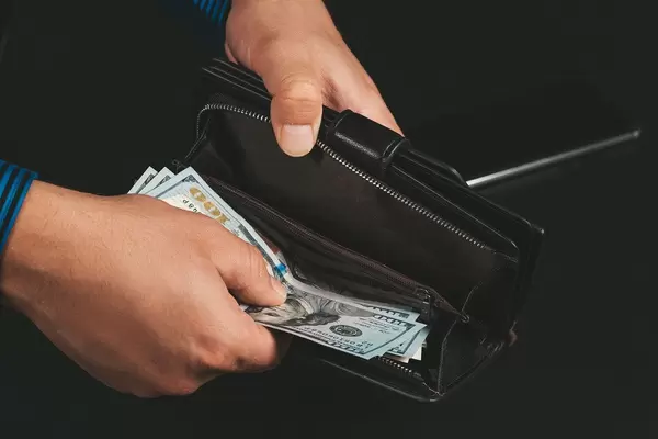 Open wallet with dollars in men's hands on a dark background