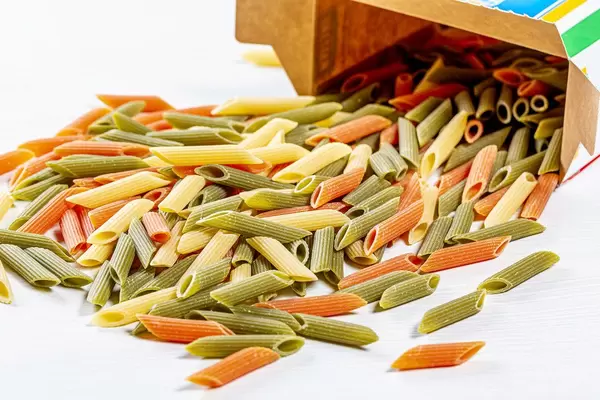 Orange, green and yellow raw pasta spilled from the box