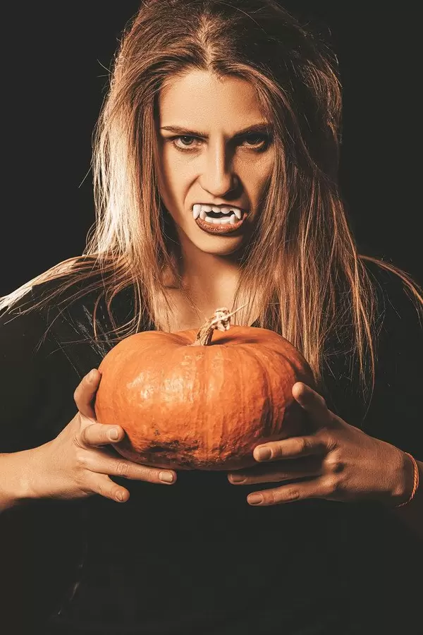 Orange pumpkin in the hands of a vampire woman on dark