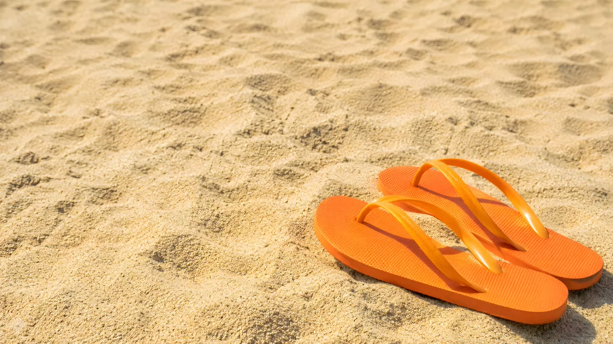 Orangefarbene Flipflops auf warmem Strandsand
