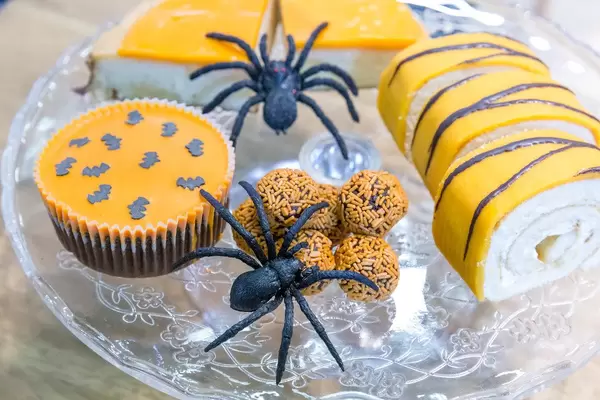 Orangefarbene Halloween Süßigkeiten mit Deko-Spinnen auf Glasteller