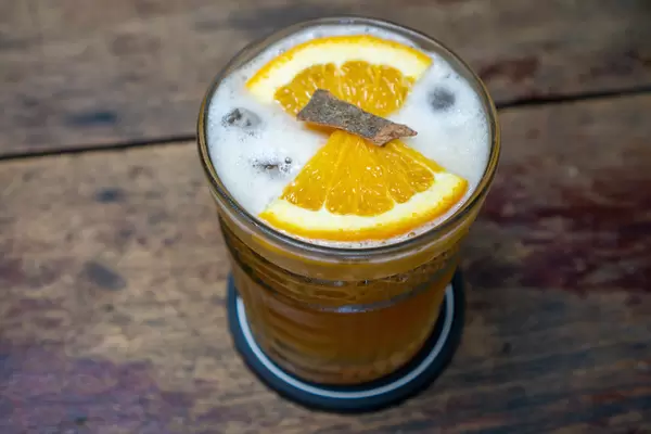 Orangen-Zimt Eistee mit frischen Orangenscheiben und Zimtstange auf einem Holztisch Nahaufnahme